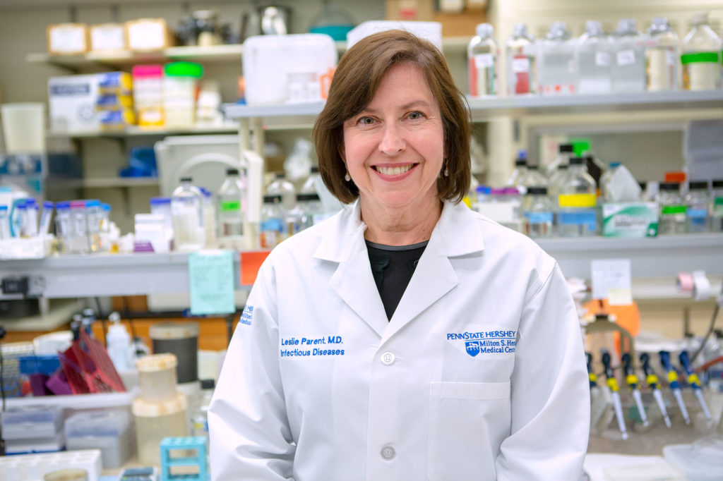 Dr. Leslie J. Parent stands in her laboratory at Penn State College of Medicine, with laboratory equipment visible in the background. She is smiling and wearing a white medical coat.