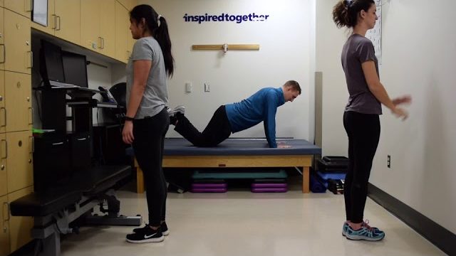 A still from a video shows three people performing the Pushup Varieties exercise.