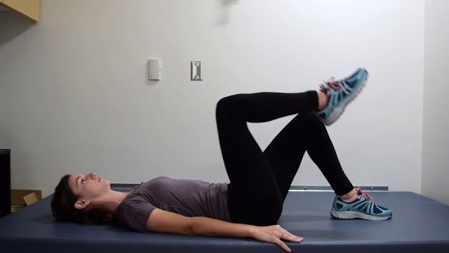 A still from a video shows a person performing the Supine Leg Marches exercise.