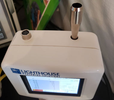 A Lighthouse 3016 Particle Counter device is seen sitting in the middle of a room.