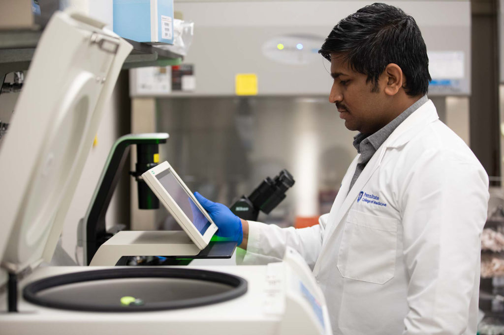 Dr. Ashwinkumar Subramenium Ganapathy in a white coat looking down at a machine in a lab.