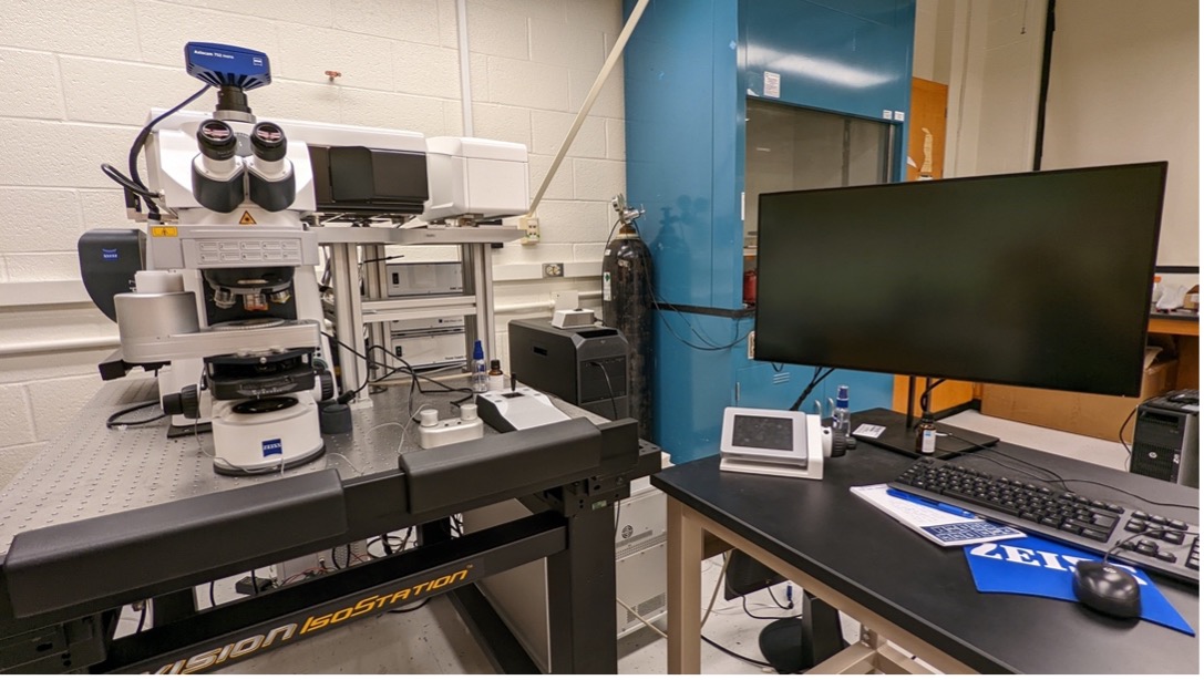 A cryo confocal microscope on a table at left, with another table at right containing a monitor, keyboard and computer mouse.