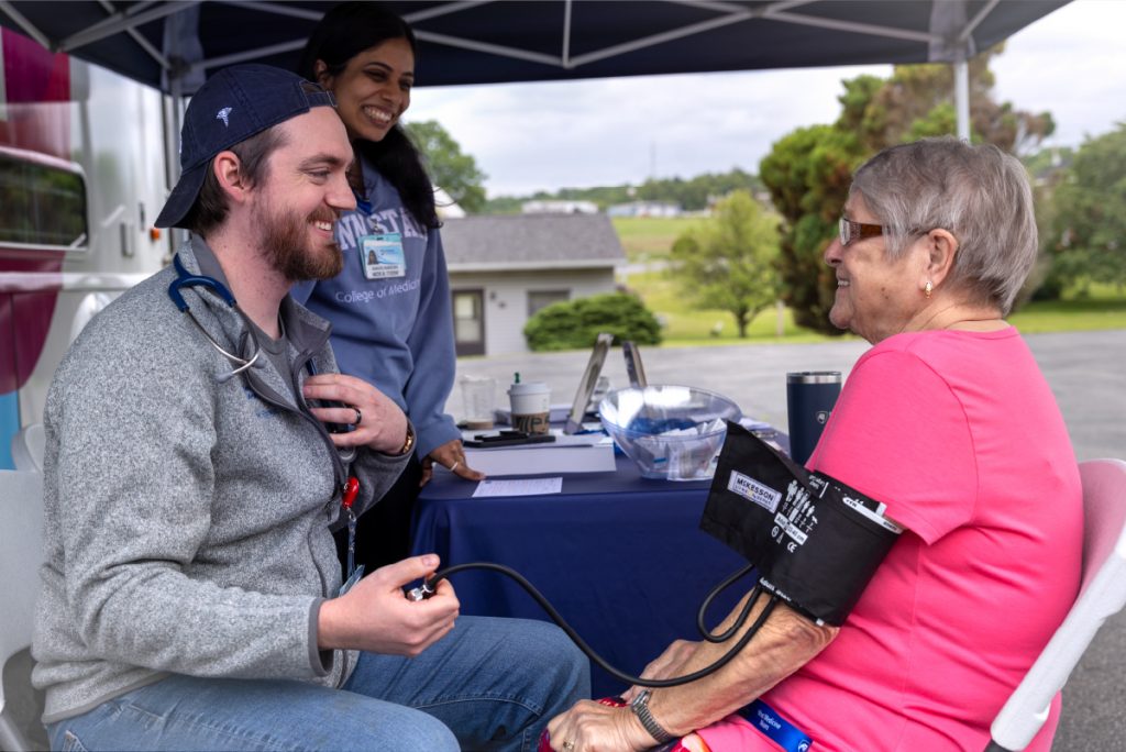 A medical student checks a woman's blood pressure under a LION Mobile Clinic tent.