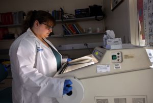 Reba Chivari looking down at a lab machine while holding a wheel on the side of it, with a darkened area in the background